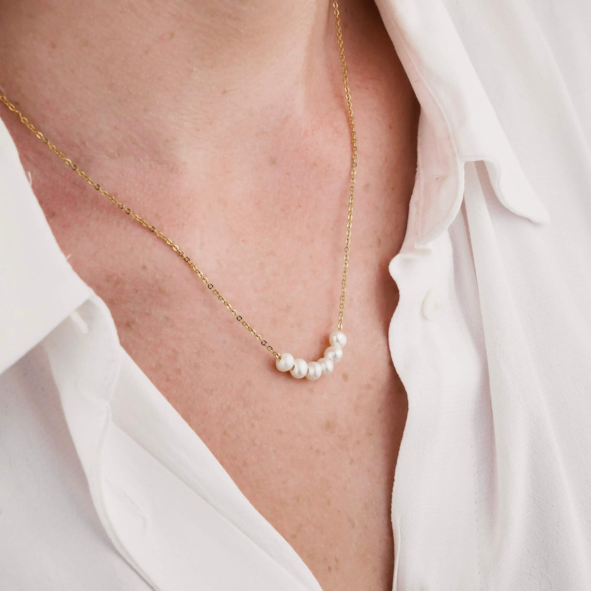 the model is wearing a pearl necklace.  the necklace is elegant and timeless. it has a dainty gold chain which holds 6 fresh water pearls. the pearls can move freely along the chain. 