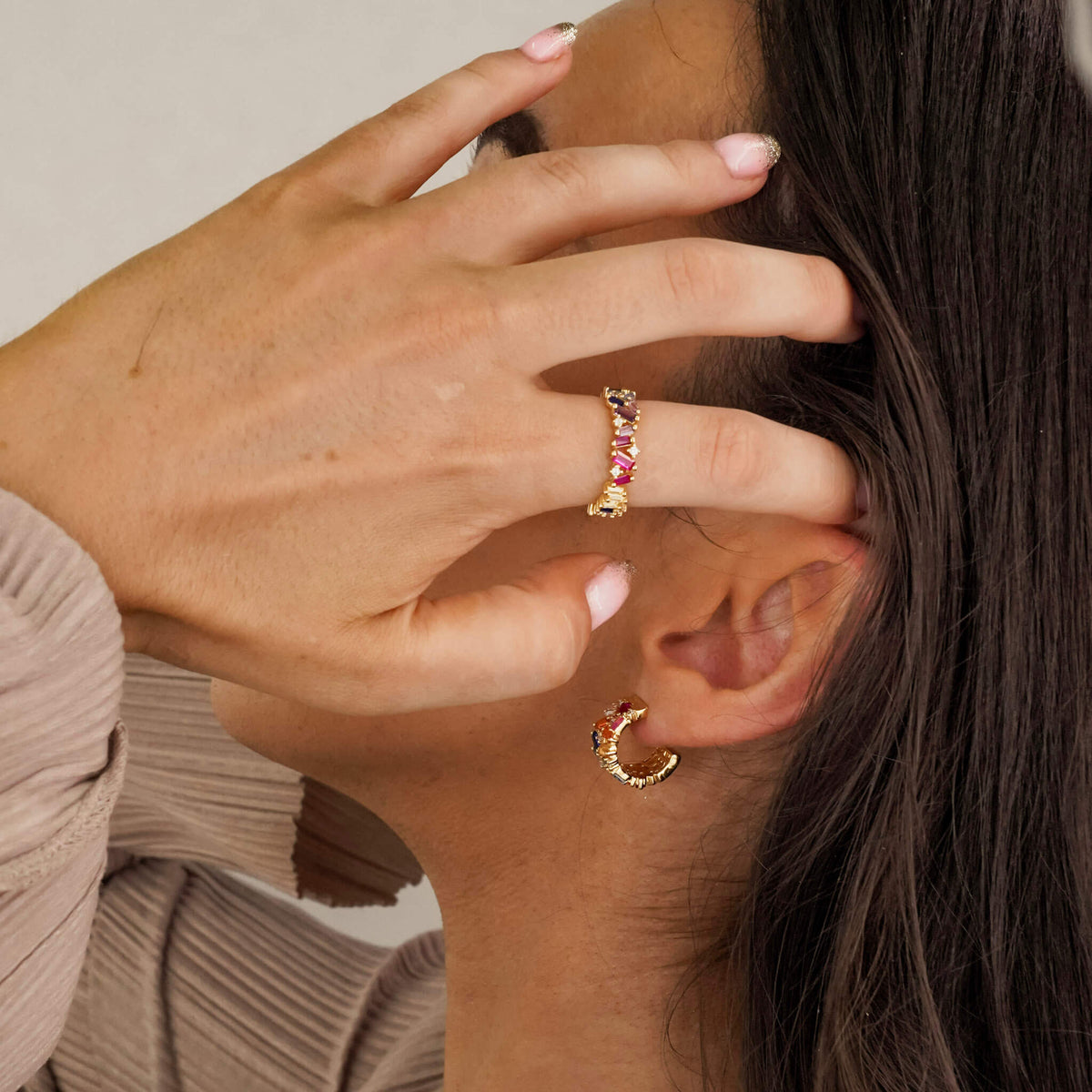 a model is wearing  the Multicoloured adorn ring from an Irish jewellery brand. The adorn ring is a colourful piece of jewellery. The sterling silver band is surrounded and covered in multicoloured zirconia stones which are set in unique and random ways.  The model is also wearing the matching Regalia hoop earrings. 