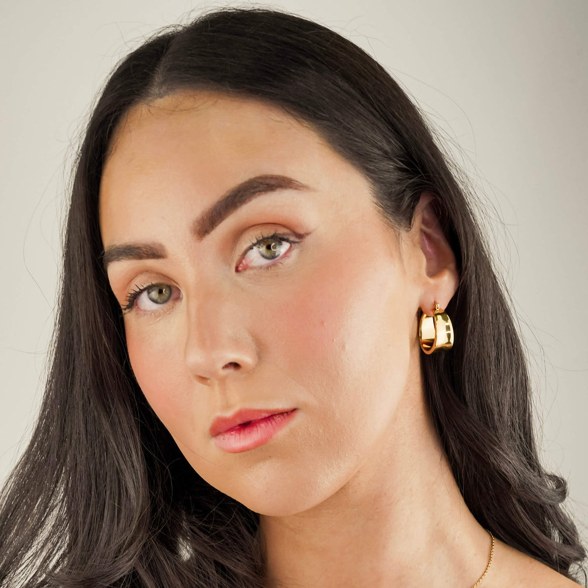 the model is wearing chunky statement earrings called the assertion hoops. They are lightweight and comfortable to wear, despite their commanding size. These earrings have a unique design that mirrors a cuff. 
