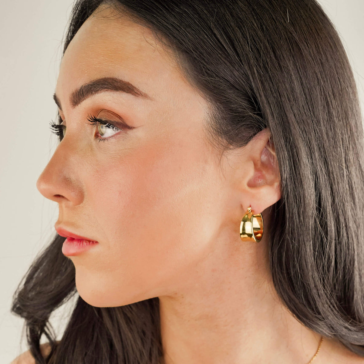the model is wearing chunky statement earrings called the assertion hoops. They are lightweight and comfortable to wear, despite their commanding size. These earrings have a unique design that mirrors a cuff. 
