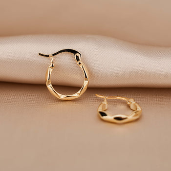 Gold hoop earrings made from high quality sterling silver plated in 18 karat gold. They have a subtle twist design. The earrings are hanging from a fine, dainty gold chain in front of pink silk.