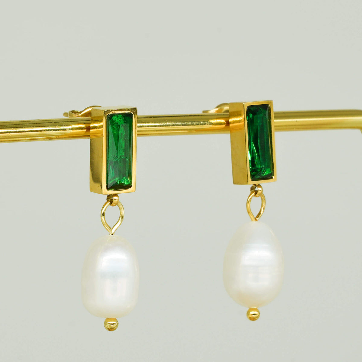 elegant earrings with an emerald stone with a dangling pearl suspended from it.