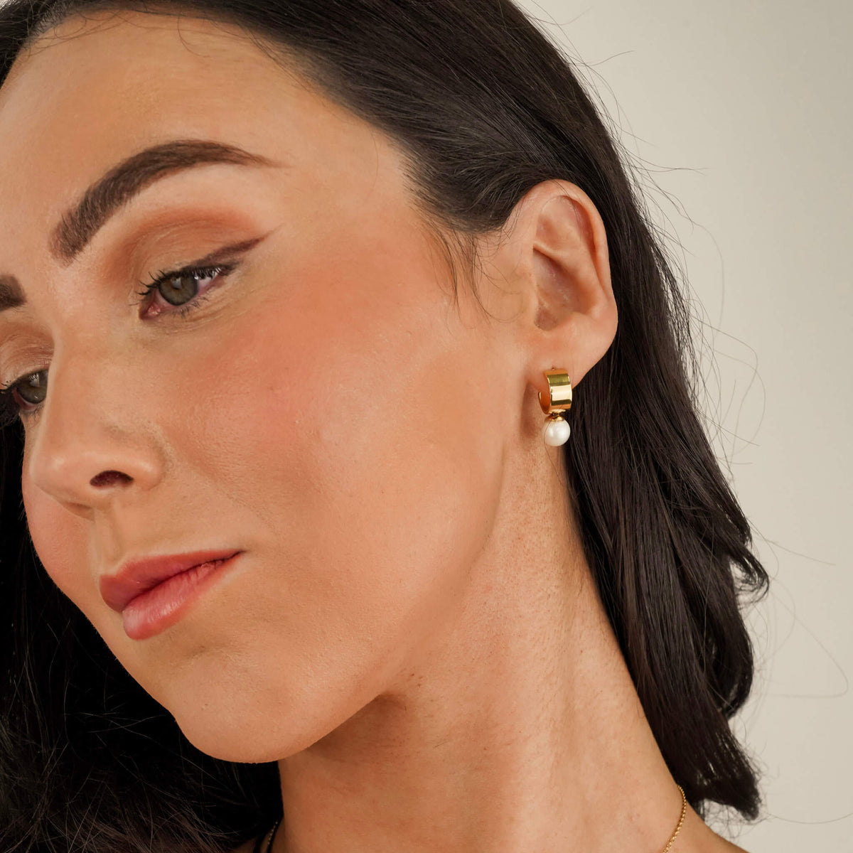 model wearing pearl earrings with a chunky gold band and the pearl fixed to the base of the hoop. 
