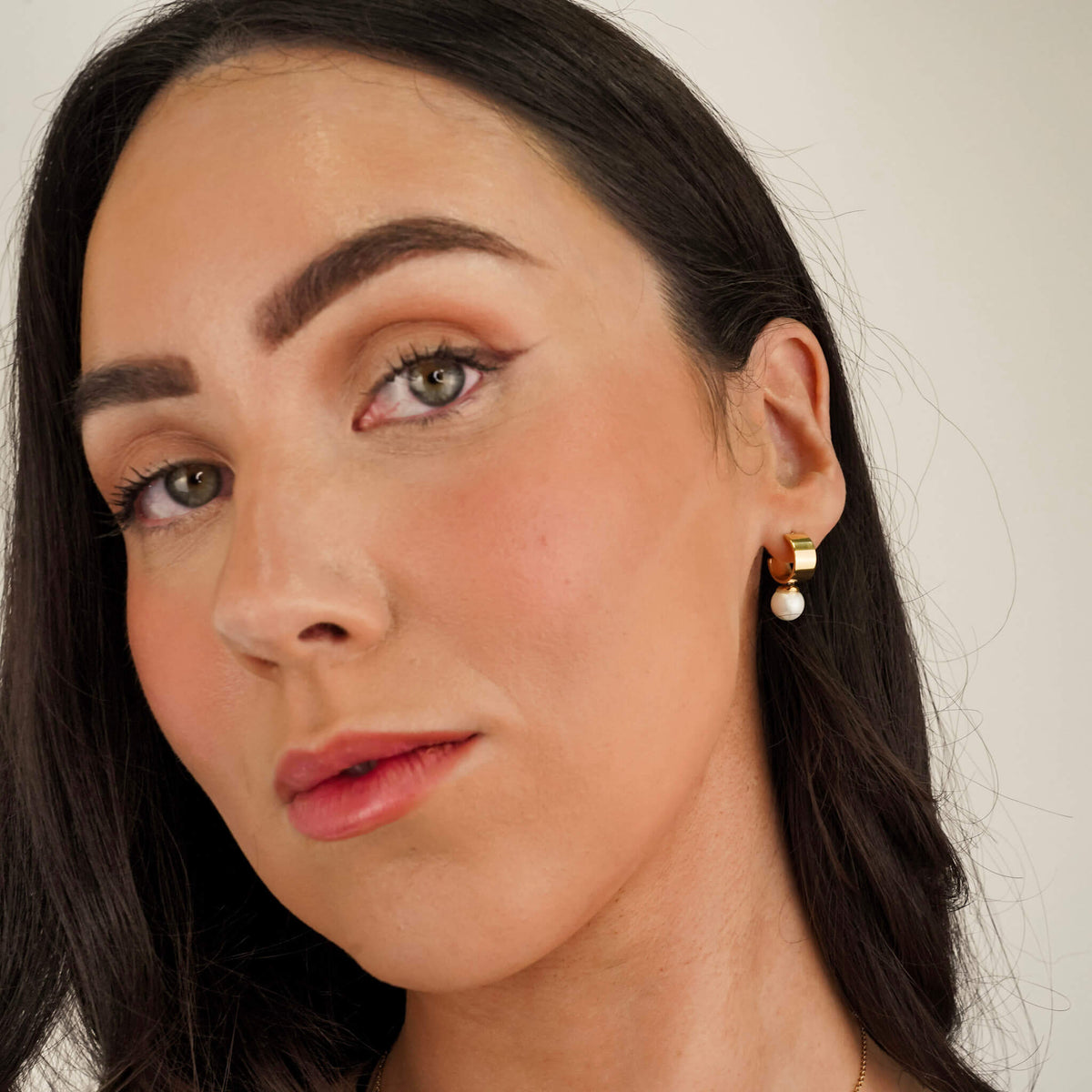 model wearing pearl earrings with a chunky gold band and the pearl fixed to the base of the hoop. 