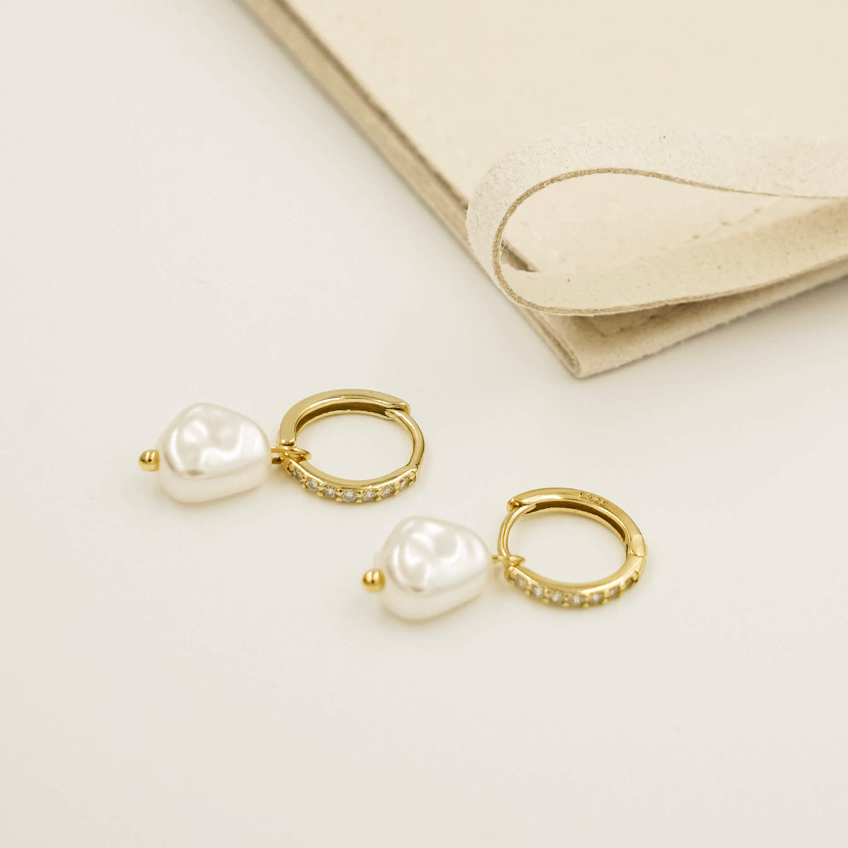 Pearl earrings with a detachable pearl charm. The charm hangs on a gold embellished huggy band.