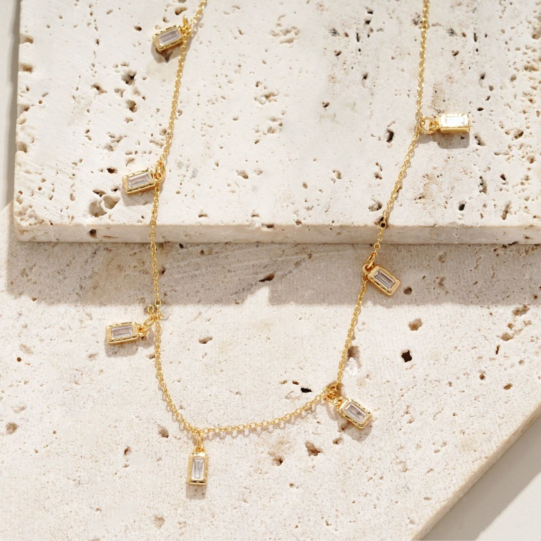 Gold necklace with rectangular pendants on a textured stone surface