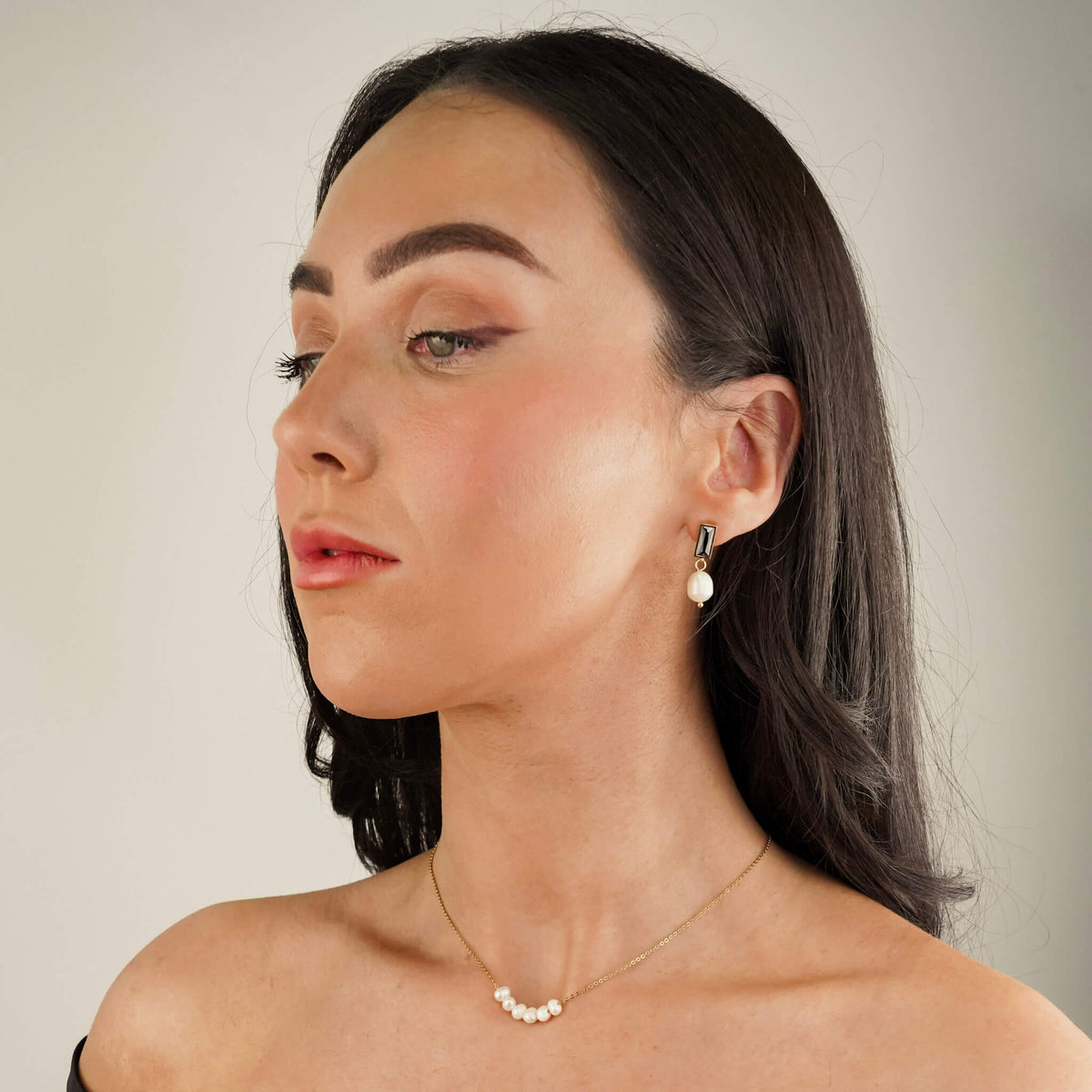the model is wearing drop style earrings. the earrings have a onyx stone stud with a pearl suspended from them. the black onyx stone and the white pearl create a sophisticated contrast. The model is also wearing the Oceanic Pearl necklace which has 6 pearls.