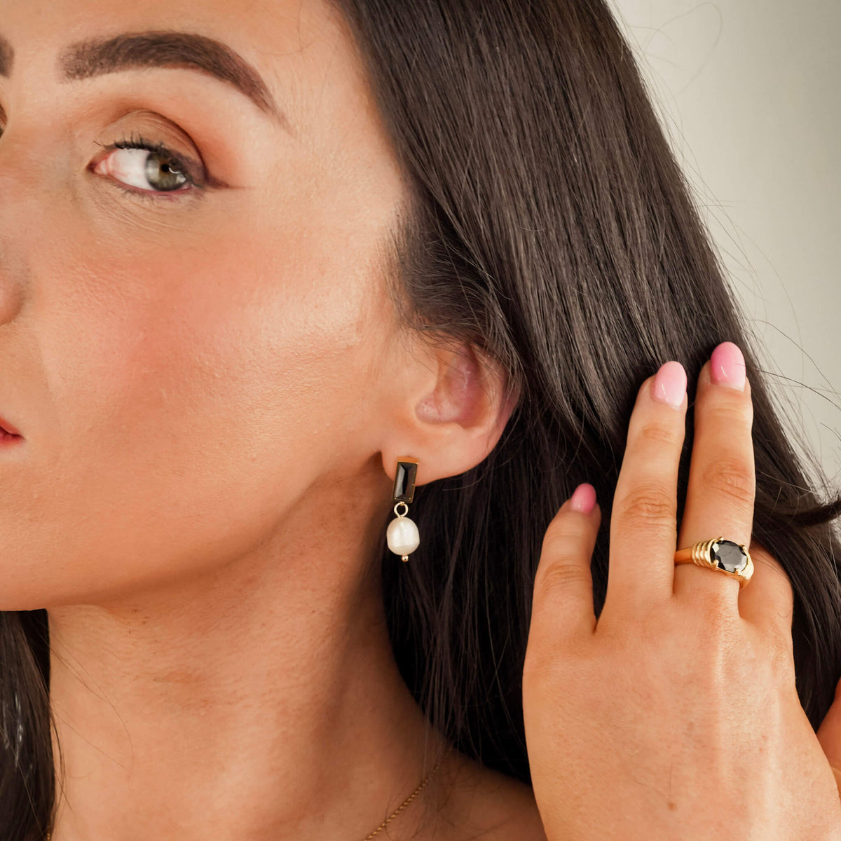 the model is wearing drop style earrings. the earrings have a onyx stone stud with a pearl suspended from them. the black onyx stone and the white pearl create a sophisticated contrast. The model is also wearing the Eclat Onyx Ring. It is a new ring with a large onyx stone at the focus.  