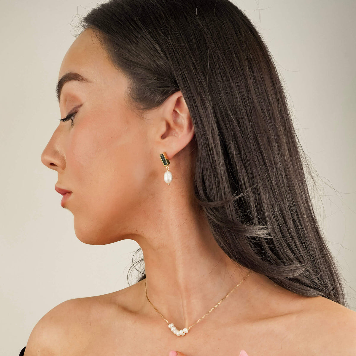the model is wearing drop style earrings. the earrings have a onyx stone stud with a pearl suspended from them. the black onyx stone and the white pearl create a sophisticated contrast. The model is also wearing the Oceanic Pearl necklace which has 6 pearls.