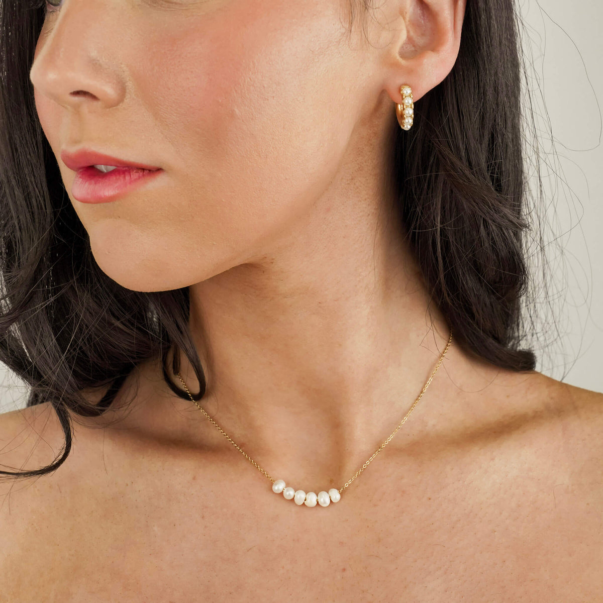 the model is wearing a pearl necklace and matching pearl hoop earrings. the necklace is elegant and timeless. it has a dainty gold chain which holds 6 fresh water pearls. the pearls can move freely along the chain. the earrings are the perfect everyday size. 