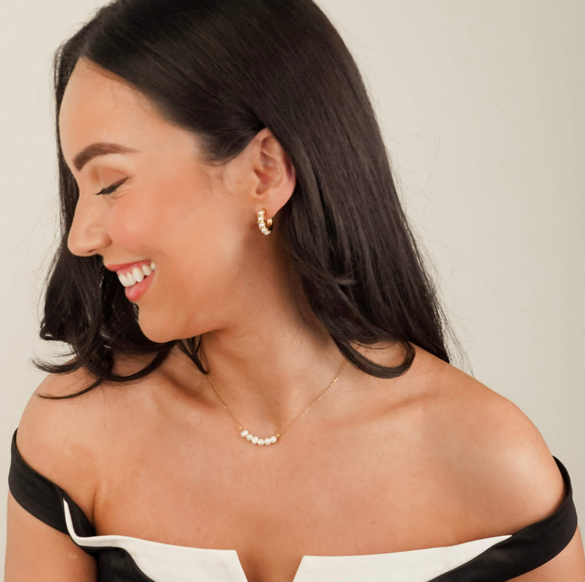 this photo shows a pearl necklace and matching  pearl earrings worn by a model. She is laughing. The pearls are bright and eye catching. The necklace has an elegant gold chain and the 6 freshwater pearls can move freely along it.  