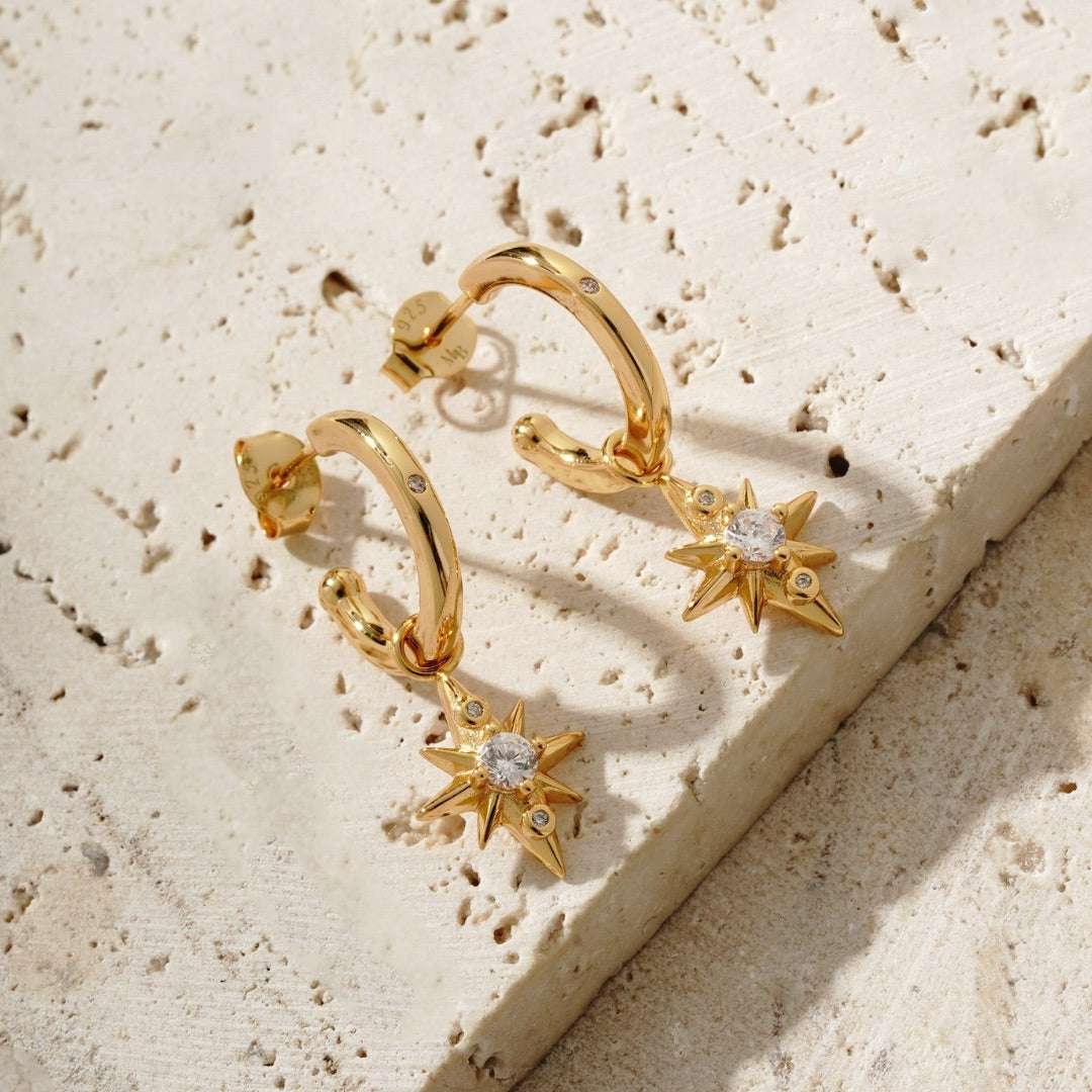 star drop earrings on a tile surface. They were designed in house by mettle and bloom. they are a hoop earring with a star suspended from it. 