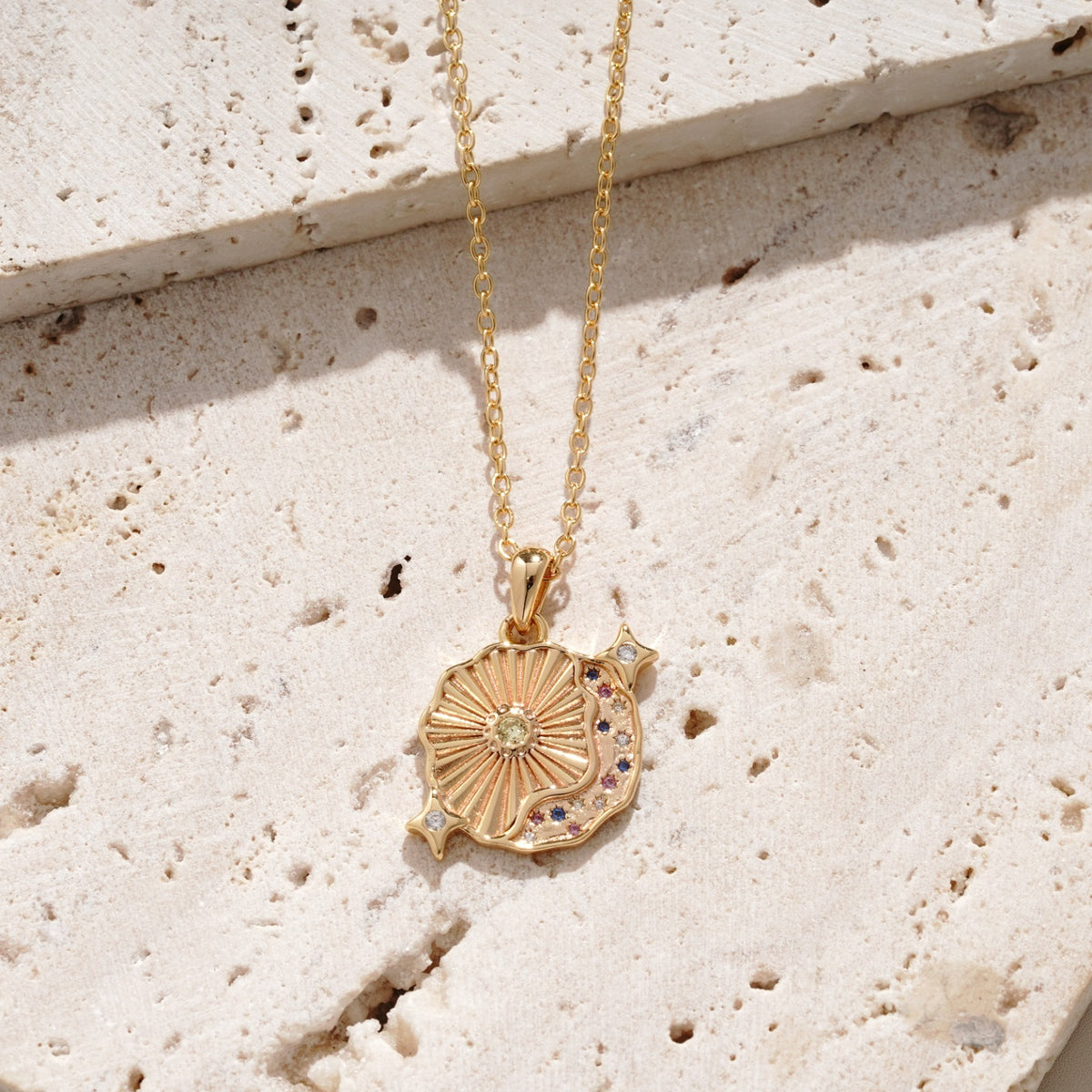 Gold undiscovered treasures necklace with a sun-shaped pendant on a textured beige surface. it's a unique and custom design by mettle and bloom. 