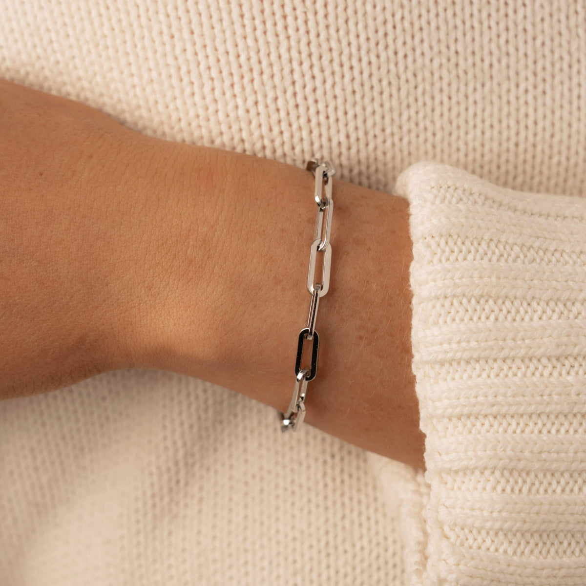 Silver waterproof link bracelet chain on a wrist against a beige background