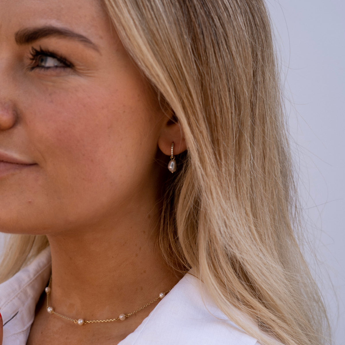 The lady is wearing the Genteel Hoop Earrings and the Panicle Necklace. The pearl earrings have a detachable pearl charm. The charm hangs on an embellished huggy band. The necklace contains beautiful pearls on a gold chain. This is perfect for a gift. 