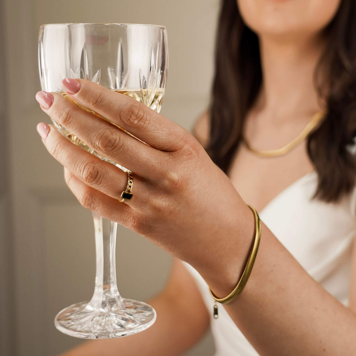 a bride is wearing a unique gold ring with a black stud on it's face while she raises her champagne glass. 