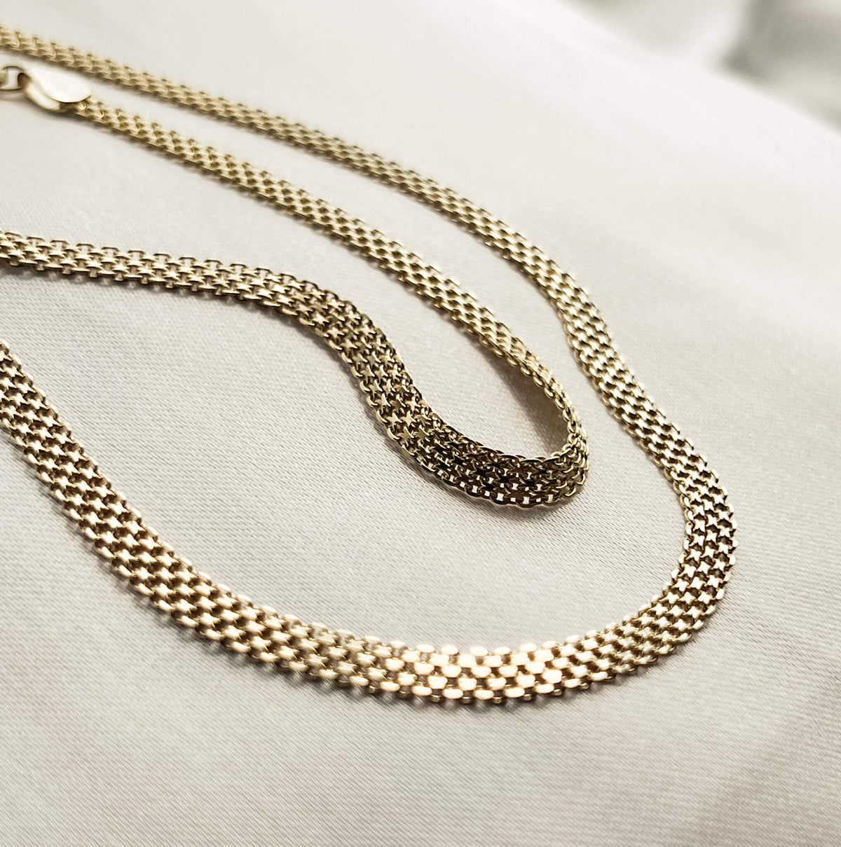 This is the gold debonair chain and the matching gold bracelet pictured on soft silk. The chain has a unique texture and design which folds in an elegant way. It has an extension clasp so it can be worn as a choker or extended. 