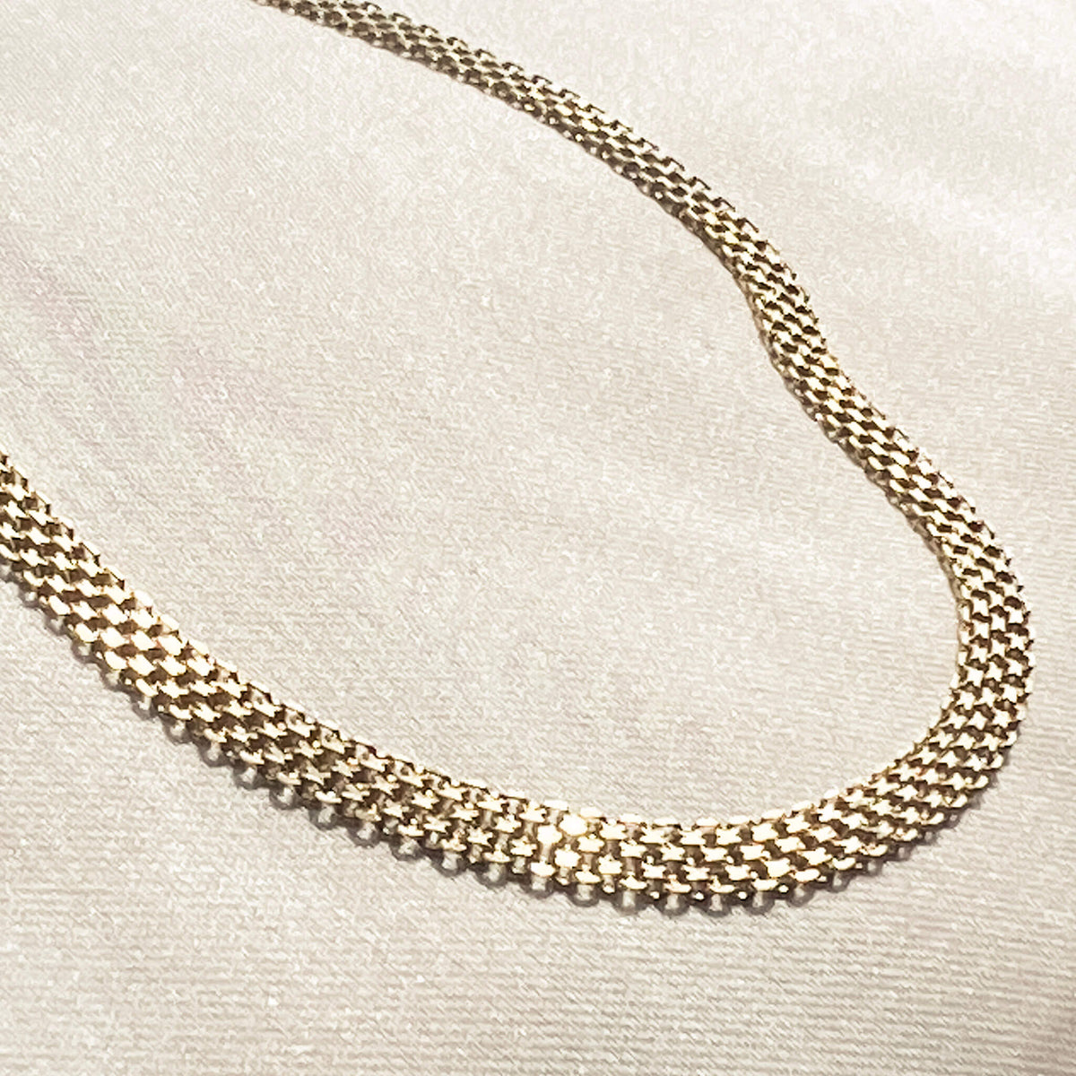 gold debonair chain on soft silk. The chain has a unique texture and design which folds in an elegant way. It has an extension clasp so it can be worn as a choker or extended. 